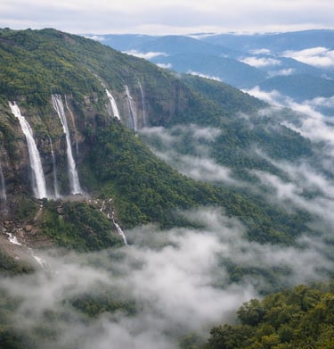 Panoramic view of the Seven Sisters Waterfalls in Meghalaya falling from lush green cliffs into a misty valley.