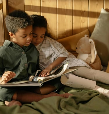 Deux enfants frères et soeurs assis sur un lit en train de lire