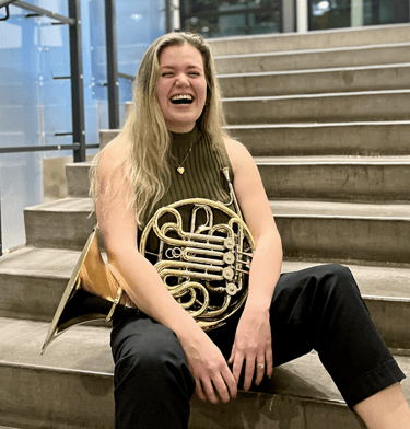 Delaney Breen sitting on a stair case with her french horn