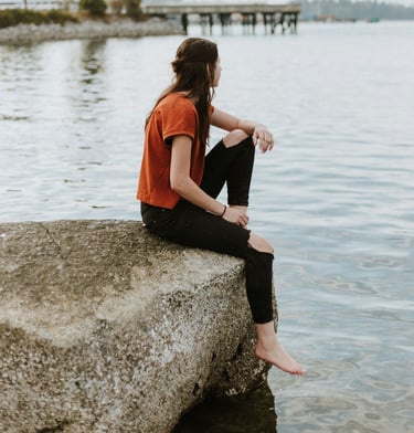 Jeune femme assise sur un rocher au bord d'un lac