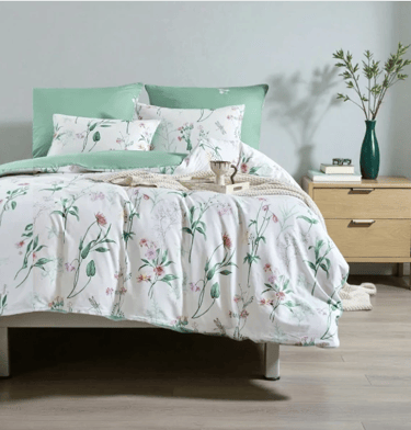 Modern bedroom featuring a white floral duvet set with sage green pillows on a wooden bed frame.