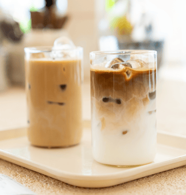 Two iced coffees on a single tray at a sunshine-soaked cafe.