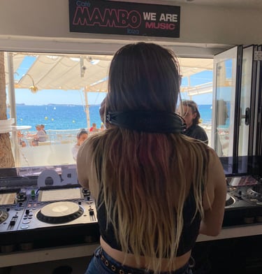 Kat Bendis performing at Cafe Mambo Ibiza booth overlooking the Mediterranean Sea and beach.