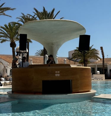 A DJ booth with a mushroom-shaped roof at a luxury pool club with palm trees.