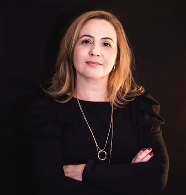 Professional portrait of a blonde woman in a black dress with crossed arms against a dark background.