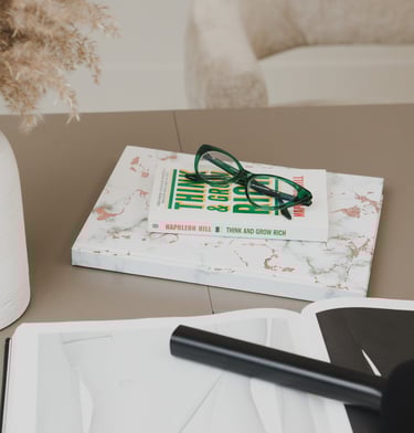Green reading glasses on a Think and Grow Rich book over a marble notebook on a desk.