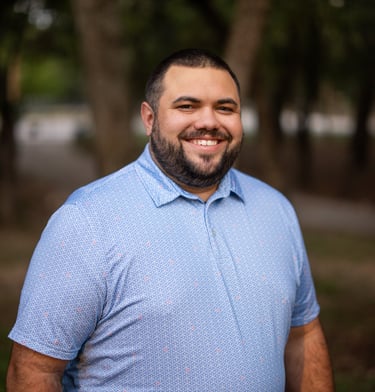 Photo of Jake Gigl smiling outdoors, wearing a blue patterned polo shirt, with trees in the background.