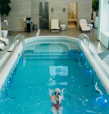 A woman swims in a luxury indoor pool at a modern spa wellness center with lounge chairs.
