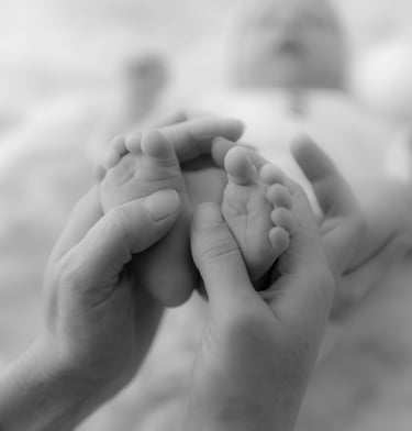 Photo en noir et blanc des pieds de bébé entourés de mains réconfortantes