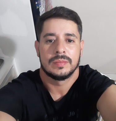 A high-angle selfie of a young man with a dark beard and mustache wearing a black t-shirt.