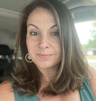 A smiling woman with brown hair and hoop earrings sitting in a car.