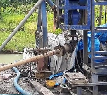 Industrial water well drilling rig operating at an outdoor construction site with pipes and machinery.