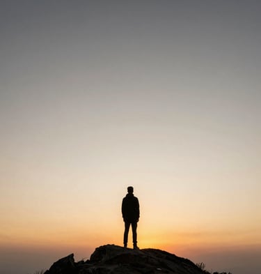 A single figure standing on a mountain peak looking at a vast, warm sunrise, expansive sky.