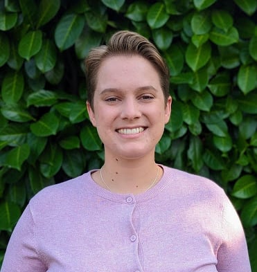 a headshot of a woman with a short haircut in front of a bush