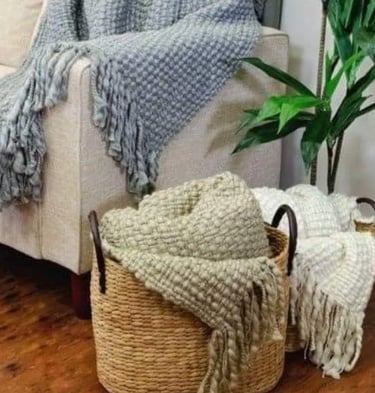 Textured knit throw blankets in a woven seagrass storage basket next to a modern sofa.