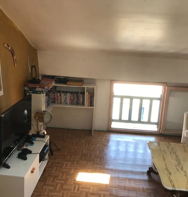 Salon mansardé avec parquet, télévision écran plat, canapé blanc et vidéothèque