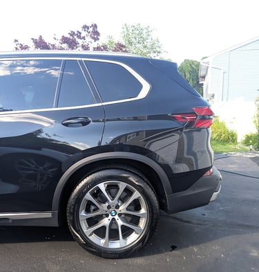 Side profile of a black BMW SUV parked on a driveway, showing the rear wheel and tail light.