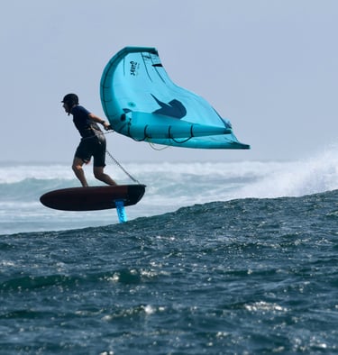 a man is holding a wing on a  foil board in the water, over a wave