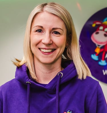Farmer Becca stood in the Moo Room smiling, holding Maggie Moo in her branded purple Moo hoodie.