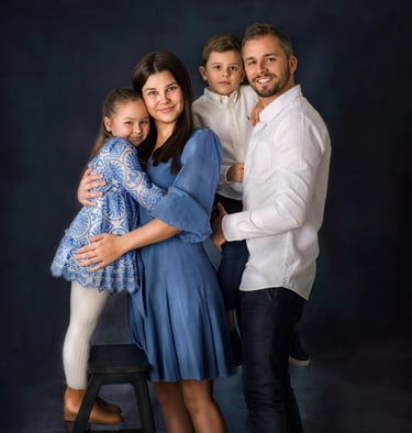 a family of four posing in a studio for a family portrait, all wearing blue and white