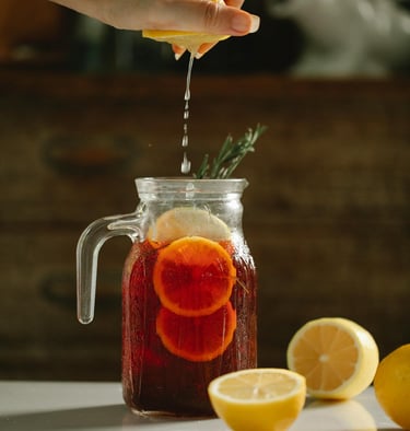 a person squeezing lemonade into a jar of cold tea