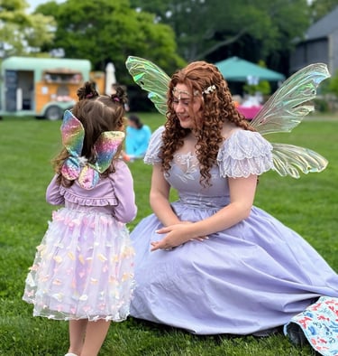 Purple fairy smiles at a kid also dressed as a fairy