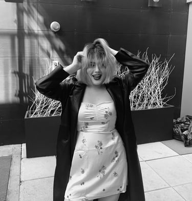 a woman (Angelina Young) in a dress and coat with a coat over her head