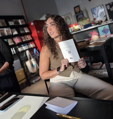 Judy sits in a bookstore holding up a designed card