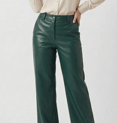 Woman wearing high-waisted dark green faux leather trousers with a cream button-down shirt.