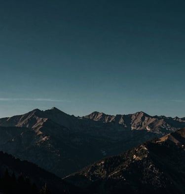A cinematic, wide landscape shot of mountains under a moody, deep midnight teal sky at dawn.