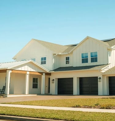 Modern residential house with large garage and landscaped front yard under a clear sky.