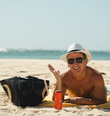 pessoa relaxando na praia em dia ensolarado com bolsa de praia e bebida refrescante