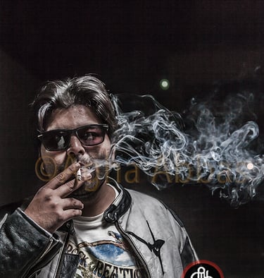 Gray-haired man in sunglasses, leather jacket, and beach t-shirt, holding cigarette with smoke, 