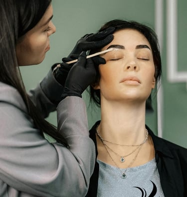 a woman is getting her eyebrows done by a professional makeup artist