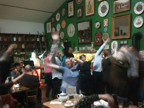 Crowd of people dancing at a lively pub with green walls decorated with vintage plates and mirrors.
