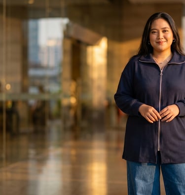 Smiling young woman in a navy blue zip-up cardigan and jeans standing in a modern building lobby.