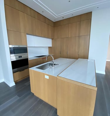 Modern luxury kitchen featuring light oak wood cabinetry, white quartz countertops, and a large island with a sink.