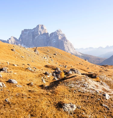 Golden autumn meadows and rocky slopes in the Italian Dolomites under a clear blue sky.