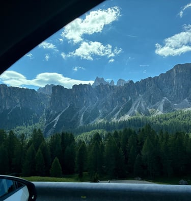 Scenic view of the jagged Dolomite mountains and pine forests in Italy from a car window.