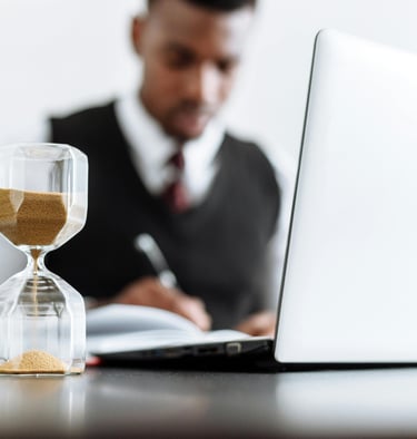 Optimiza tu tiempo con Cuvo: reloj de arena junto a persona trabajando en análisis de datos.