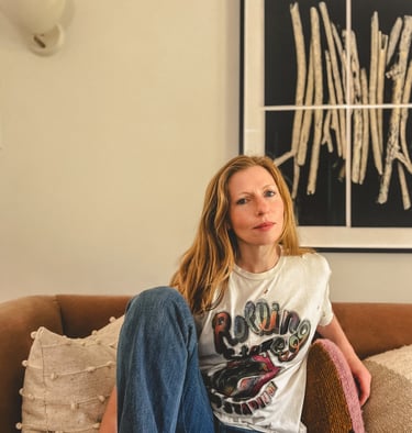 Editorial portrait of a yoga teacher with red hair and somatic practitioner, seated on a sofa. 