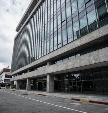 Wide architectural view of a modern corporate office in Quito, cool daylight reflecting on polished concrete and glass, structured and professional setting, generous negative space on the left.