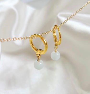 Aros de oro con gotas de piedras preciosas blancas que cuelgan de una cadena de oro sobre tela.