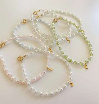 Collares de cuentas hechos a mano con perlas y dijes de luna dorados sobre una superficie blanca.