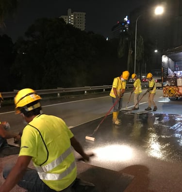 Construction workers in high-visibility vests paving a road with asphalt at night.