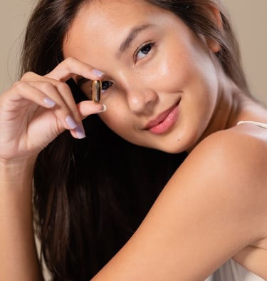 Beautiful young woman holding a vitamin supplement capsule, promoting beauty, health, and wellness.