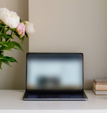 a black laptop on a desk with flowers in a vase