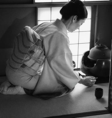 alt="Traditionelle japanische Teezeremonie: Frau im Kimono sitzt im Seiza auf Tatami-Matten und reic