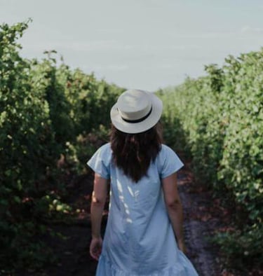 a woman in a white dress and hat walking down a path