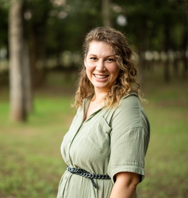 Headshot of Meg Gigl in a green dress with tress in the background